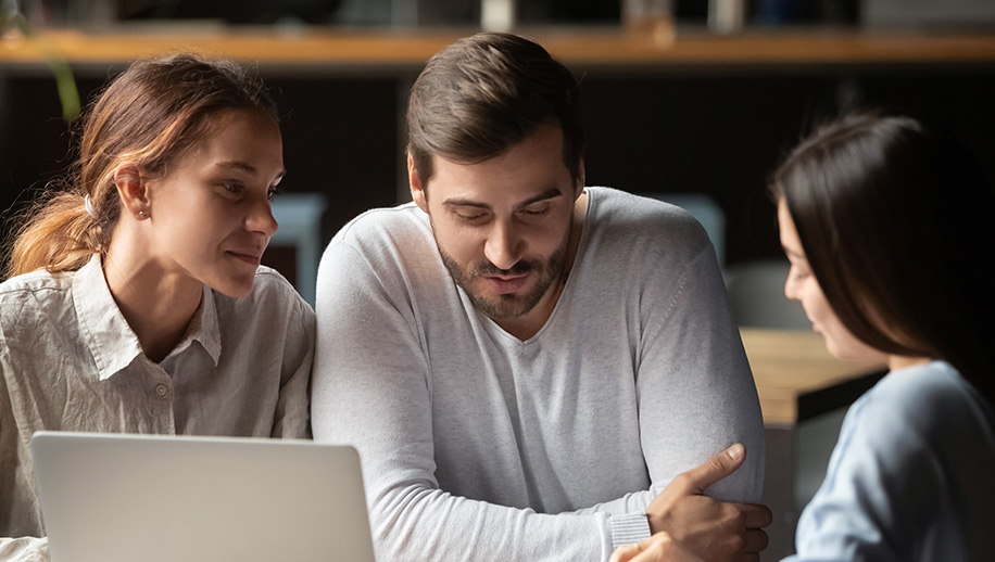 Woman showing a man and a woman something on a laptop.